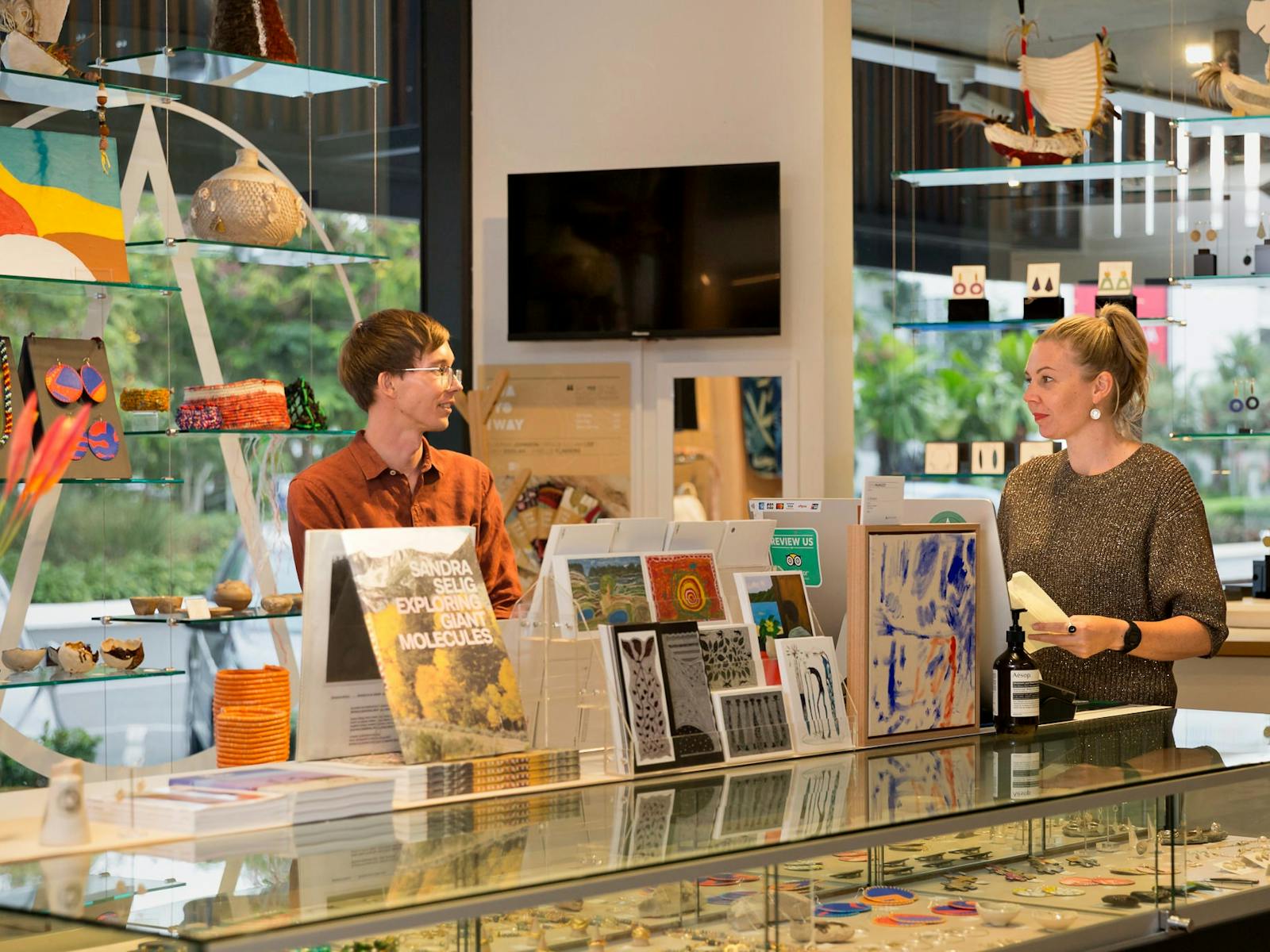 A young man and women chat at the NorthSite Store front desk, near beautiful art, cards & jewellery A young man and women chat at the NorthSite Store front desk, near beautiful art, cards & jewellery