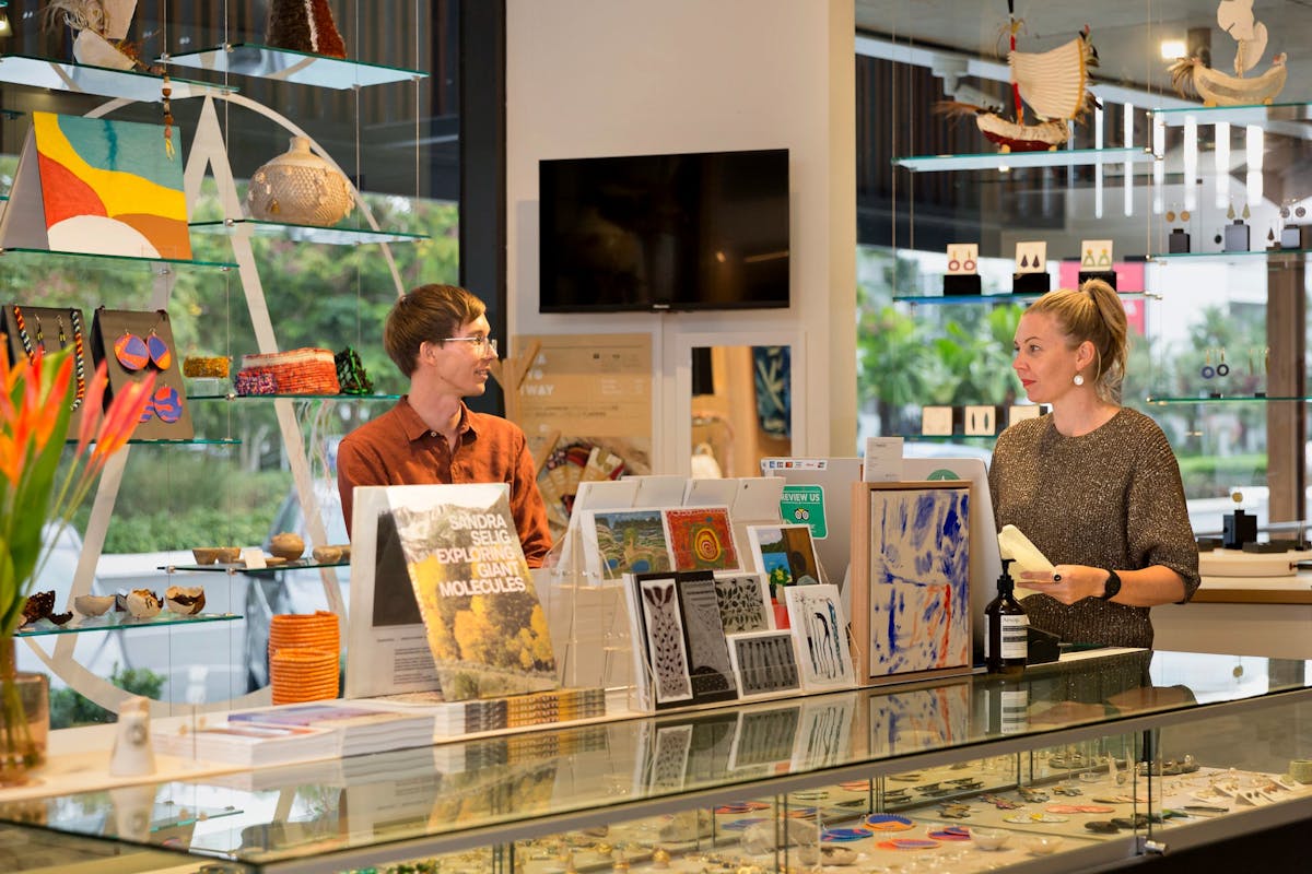 A young man and women chat at the NorthSite Store front desk, near beautiful art, cards & jewellery