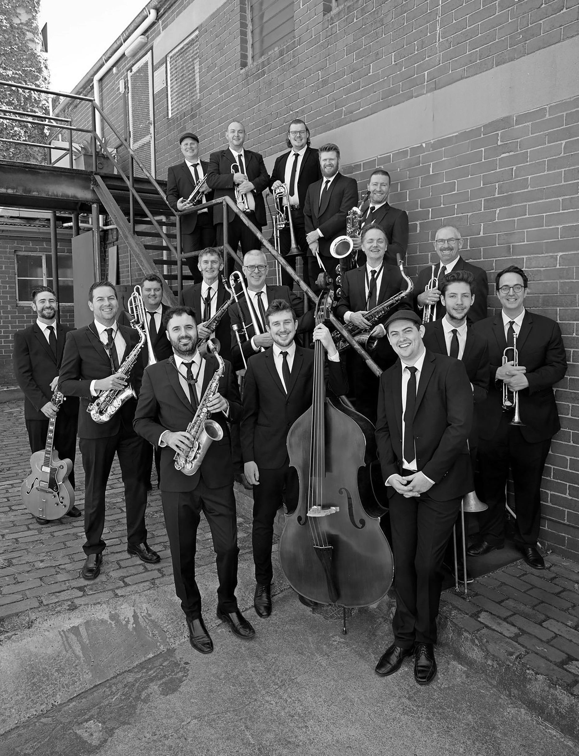 Black and white photo of seventeen jazz musicians wearing suits and smiling