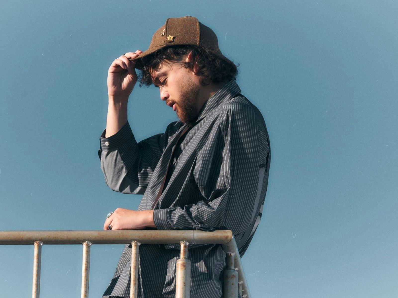 Boy Soda holds onto his cap in front of a blue sky