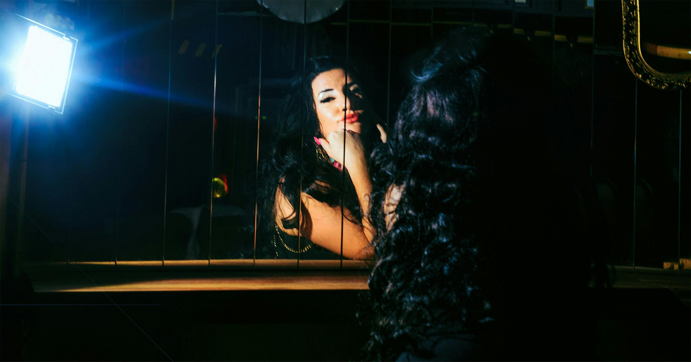 Zoe K with black clothes and hair, staring at herself in the mirror