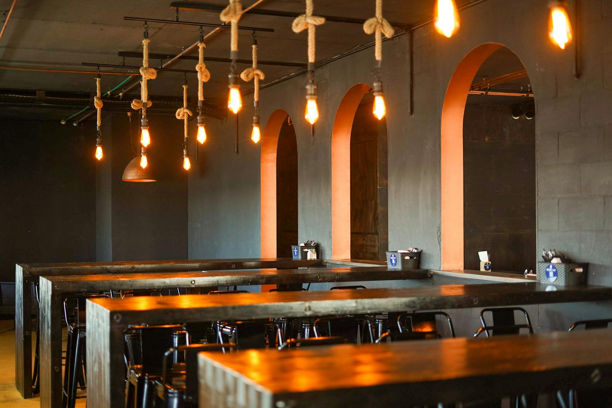 Black timber long tables accented with hanging rope lights and copper archways