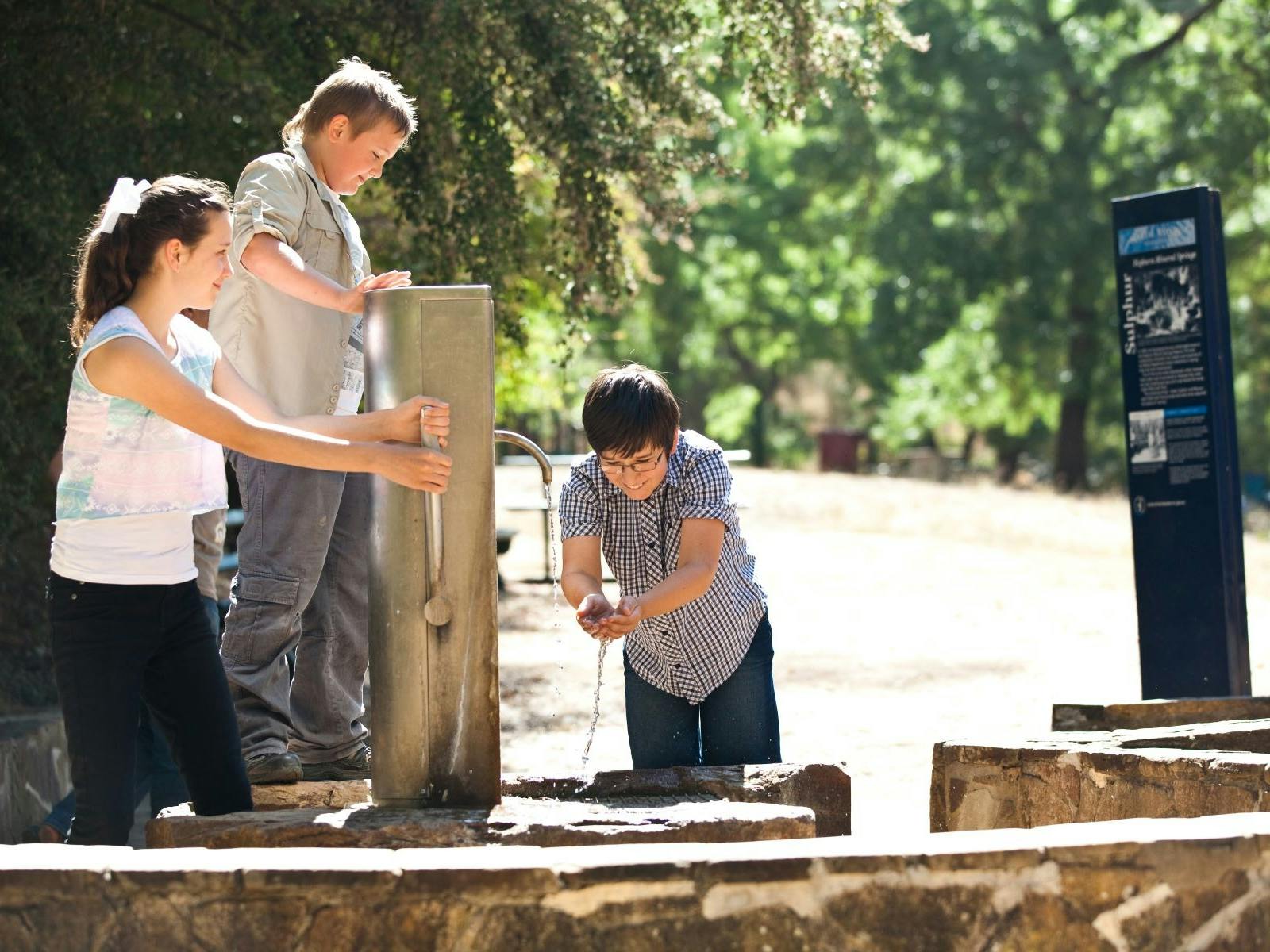 Three children tasting mineral water from the pumps