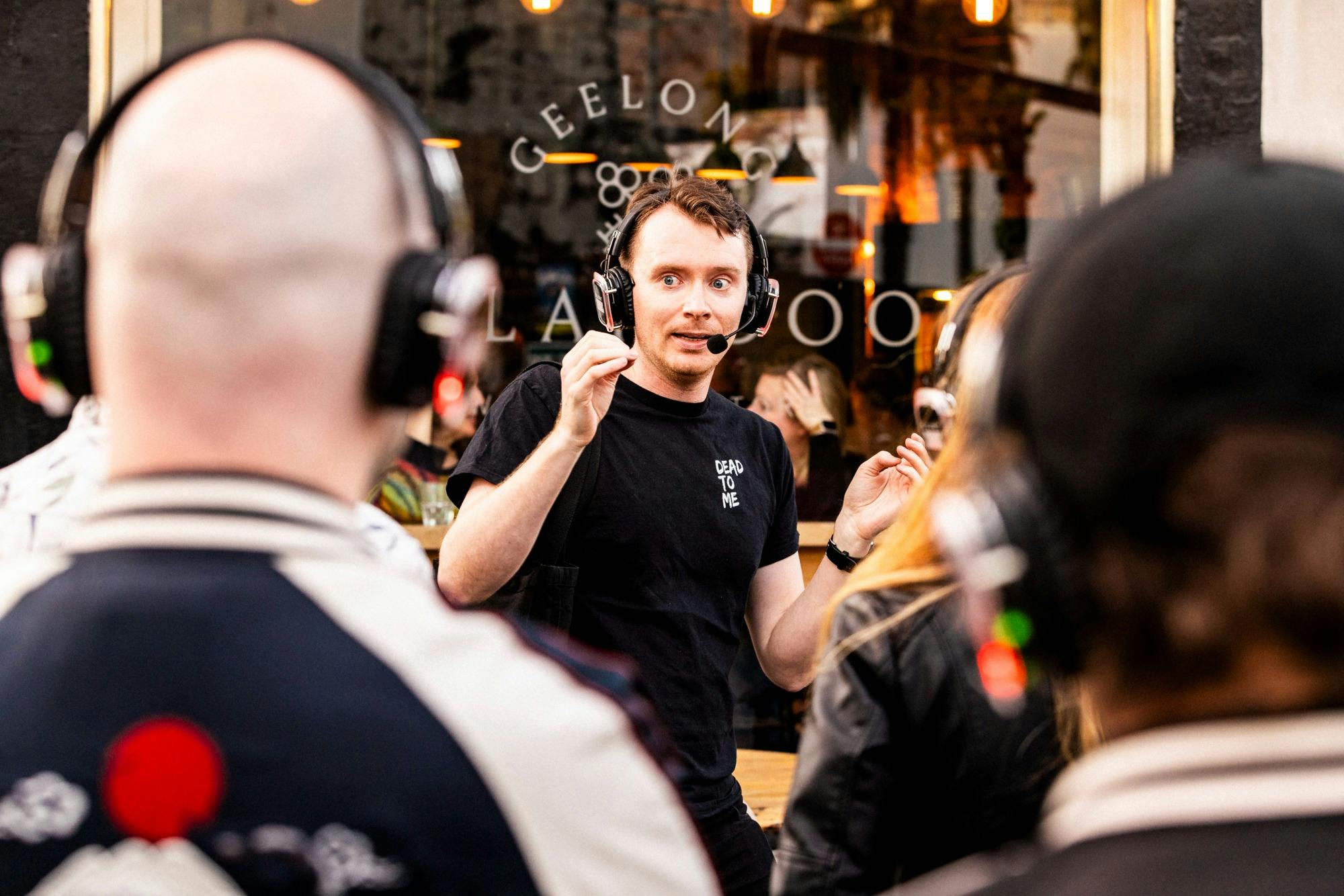 Man in black t-shirt talking to an audience with a terrified look on his face
