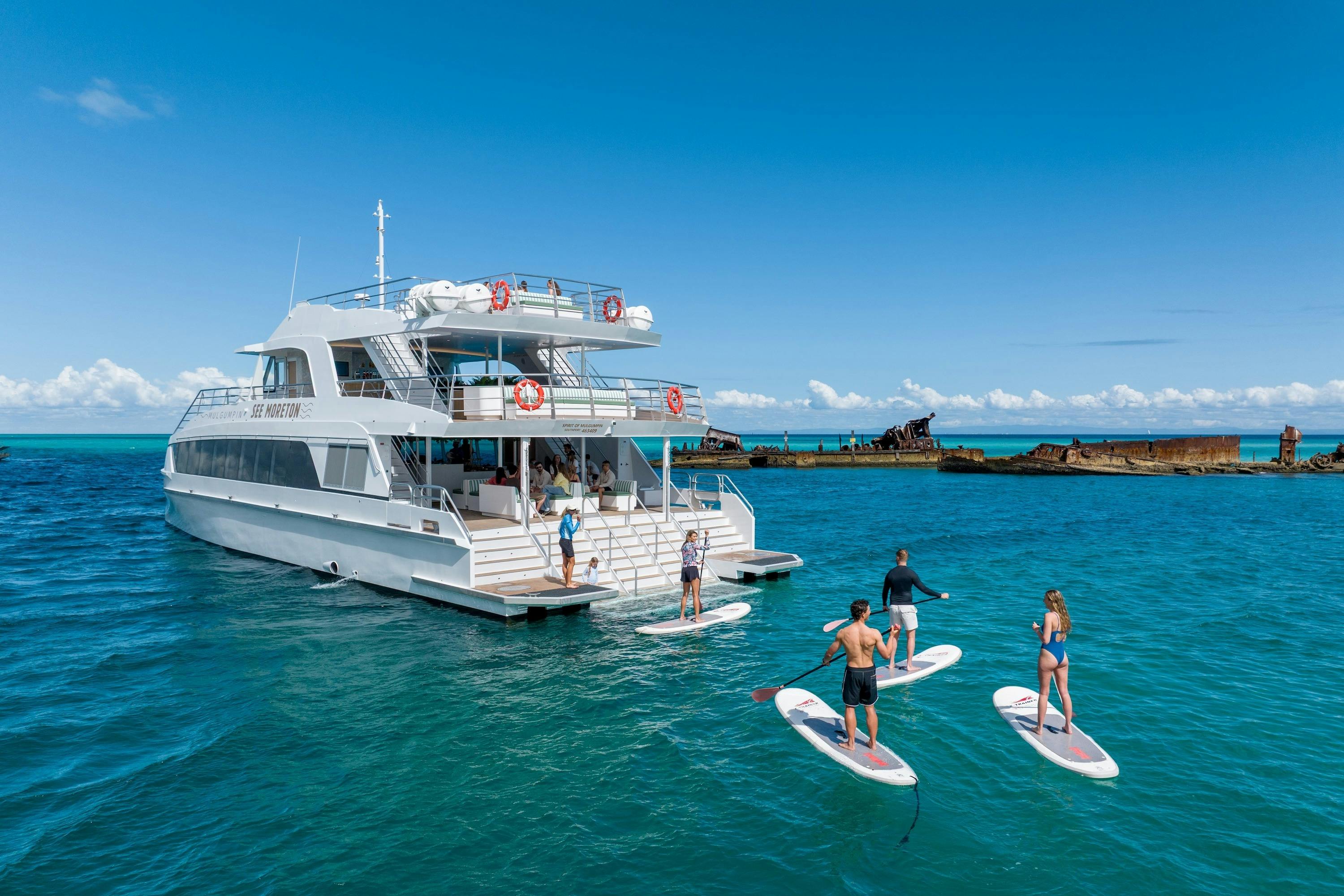 Guests enjoying stand up paddleboarding beside See Moreton and the Tangalooma Wrecks