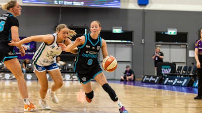 Women bounces basketball while being heavily defended.