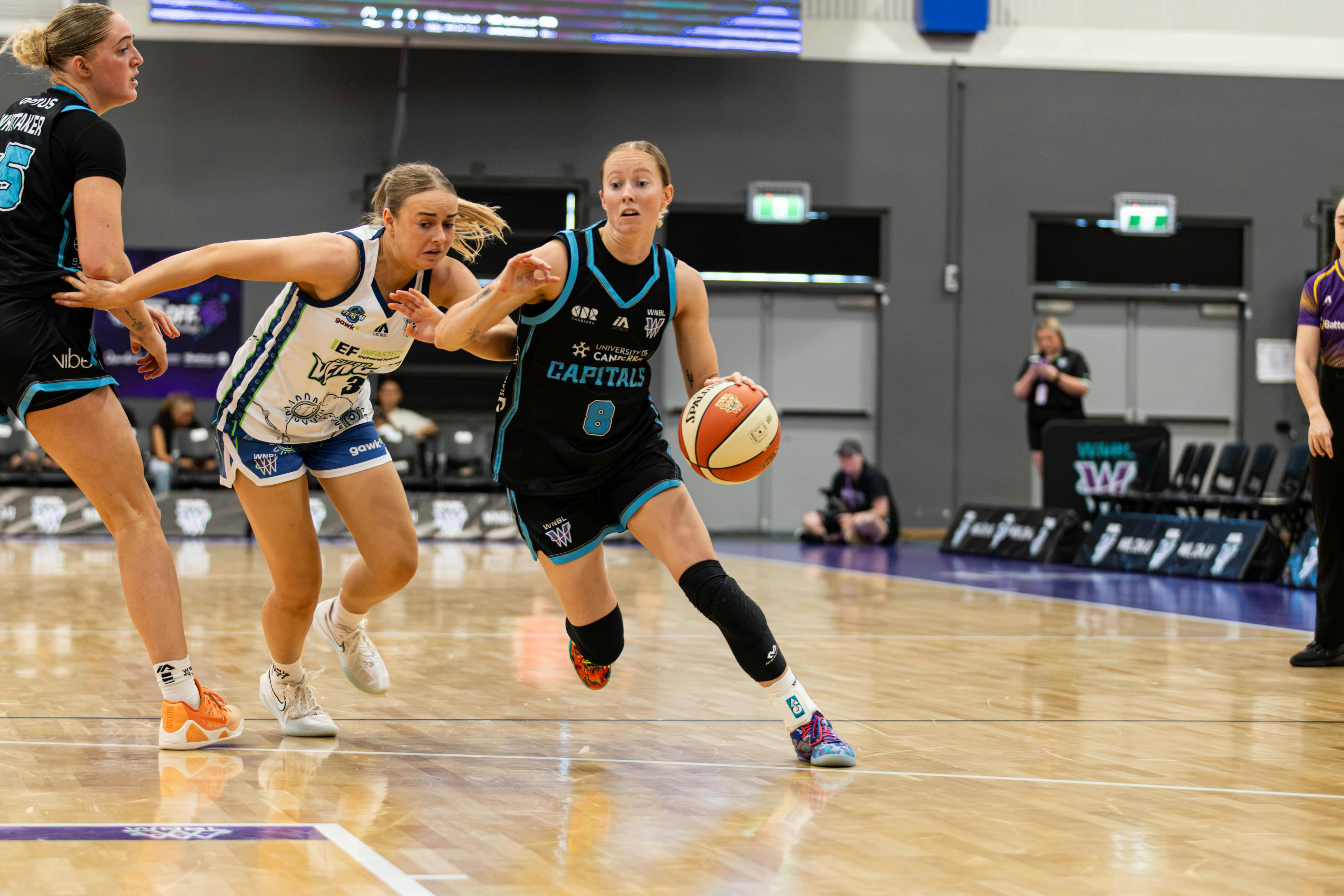 Women bounces basketball while being heavily defended.