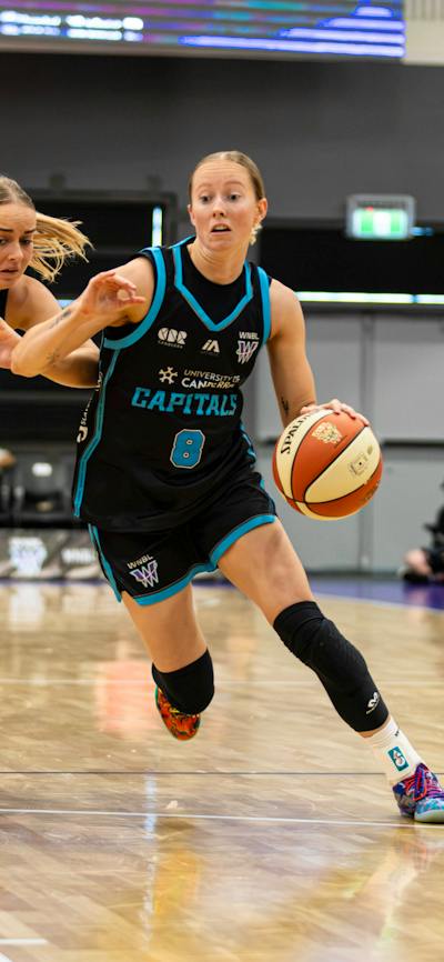 Women bounces basketball while being heavily defended.
