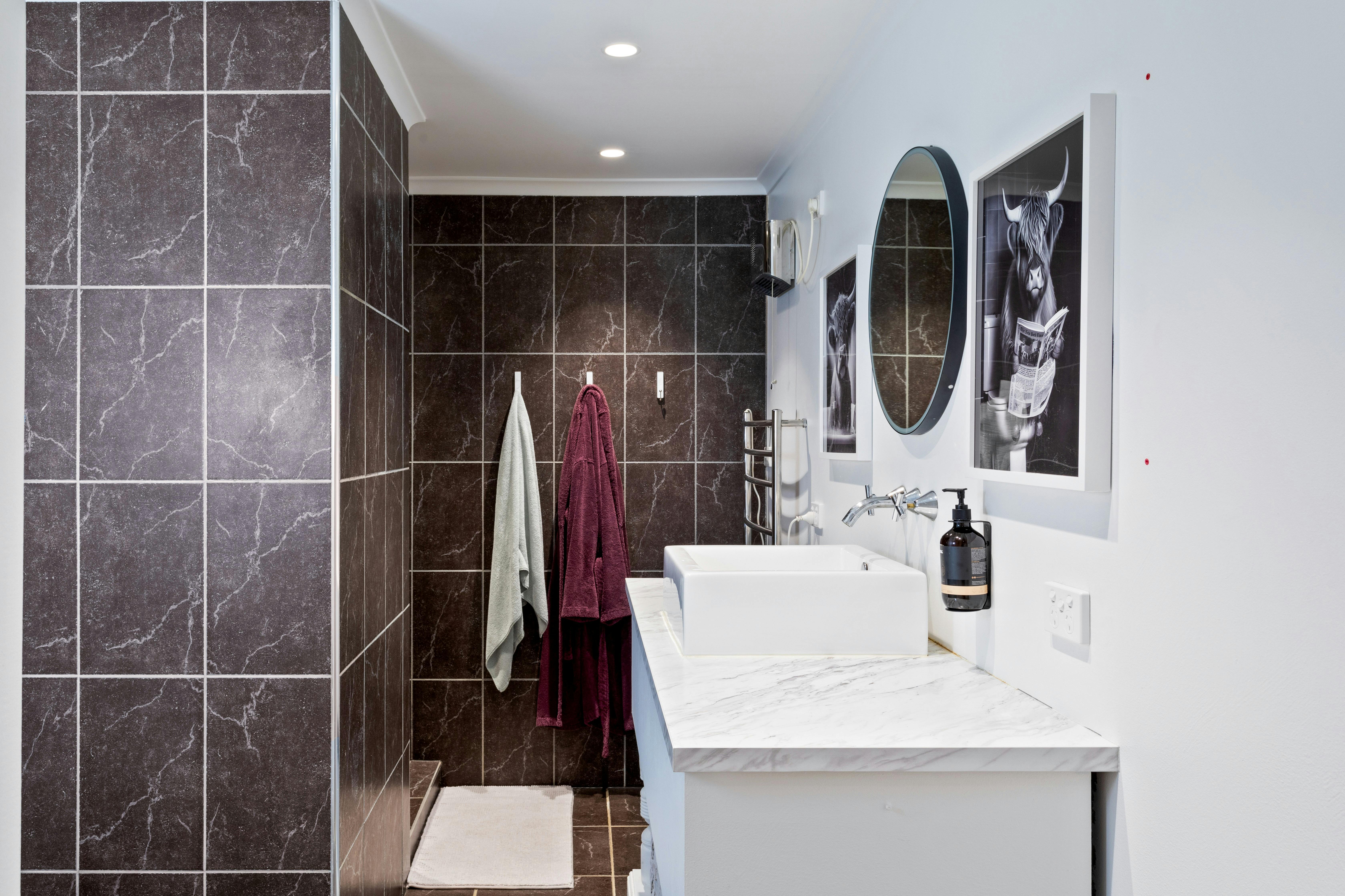 Bathroom with tiled walls showing vanity, mirror, towel and bathrobe