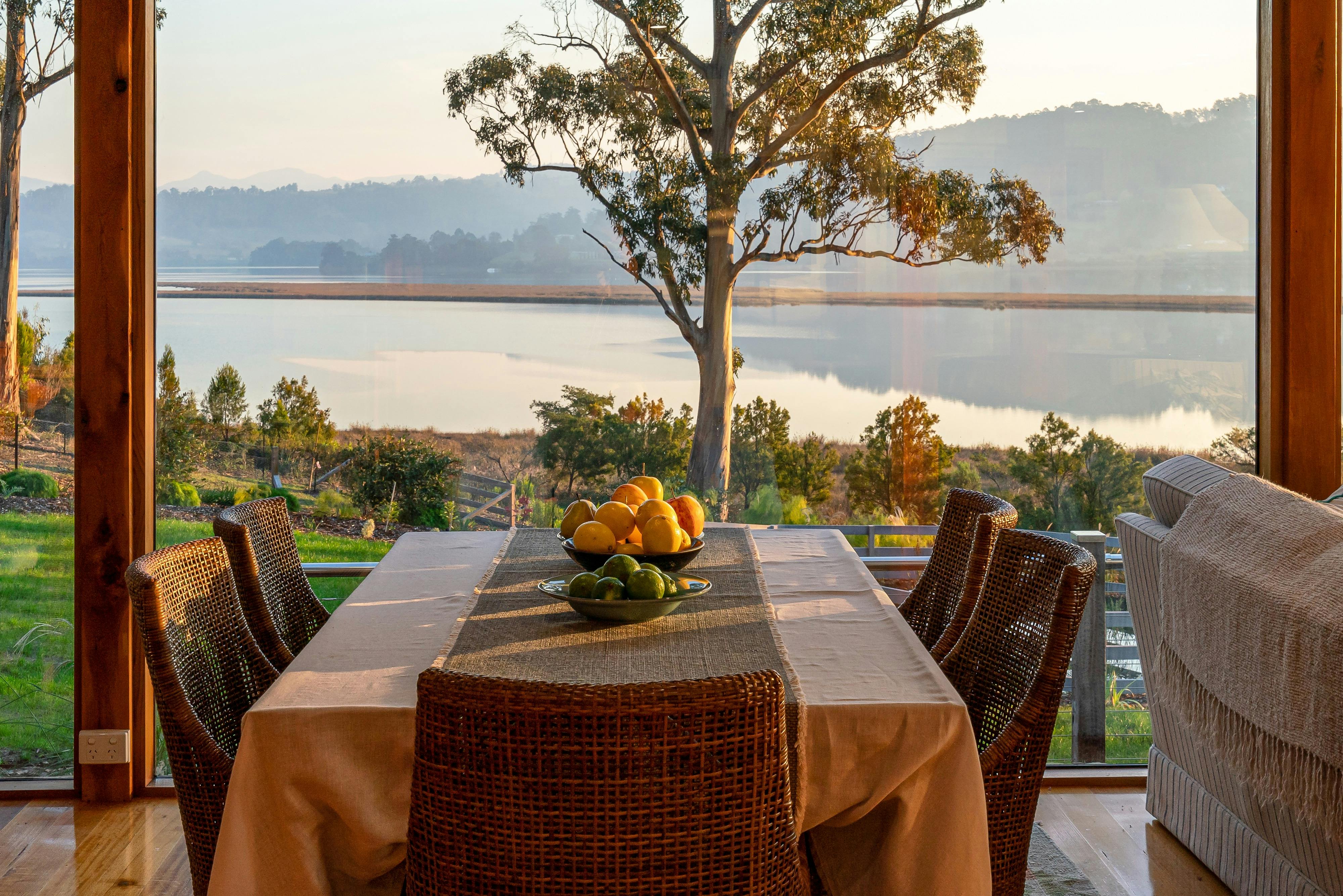 A photo of the Huon River Hideaway dining setting looking out the open windows across the Huon River