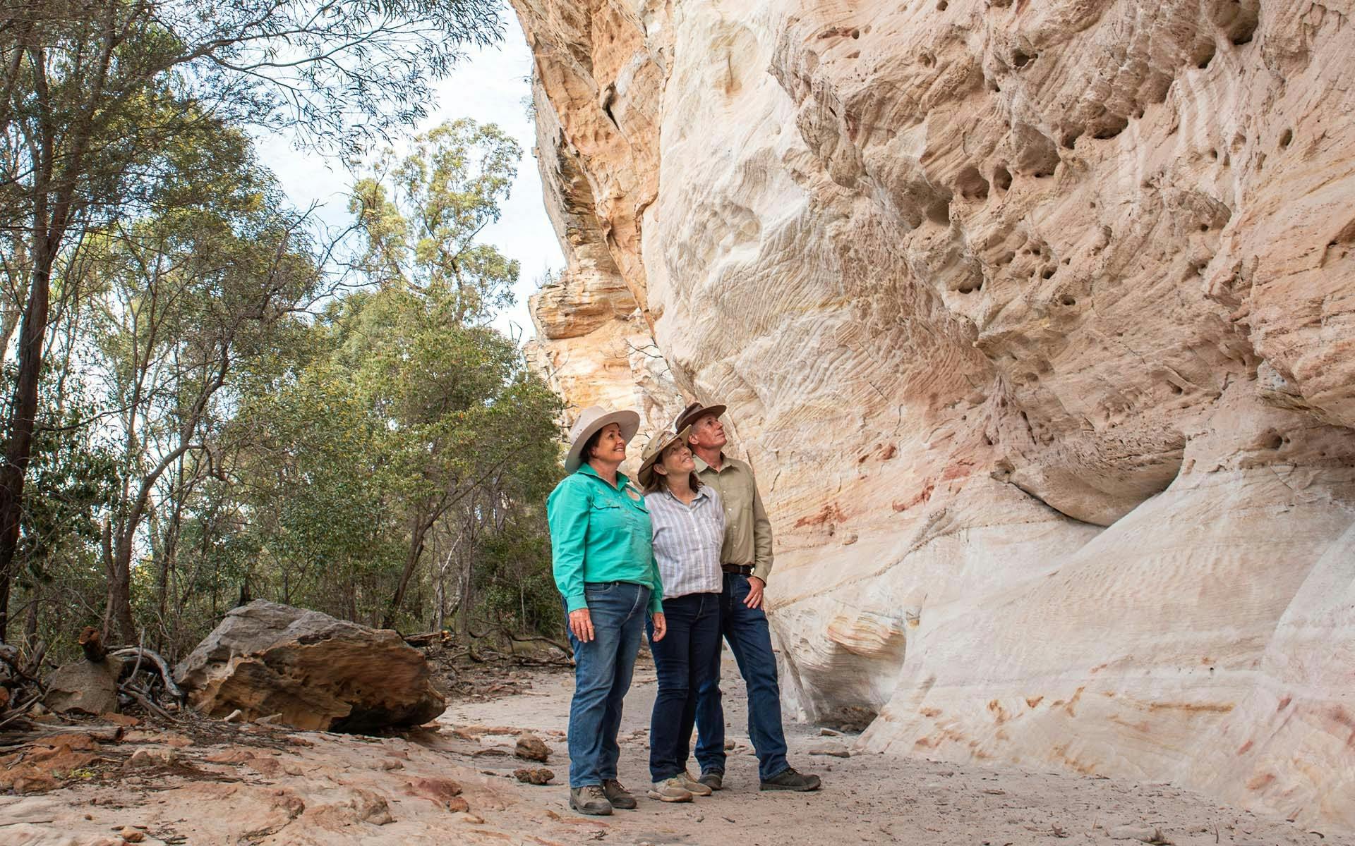three people looking up at a sandstone wall