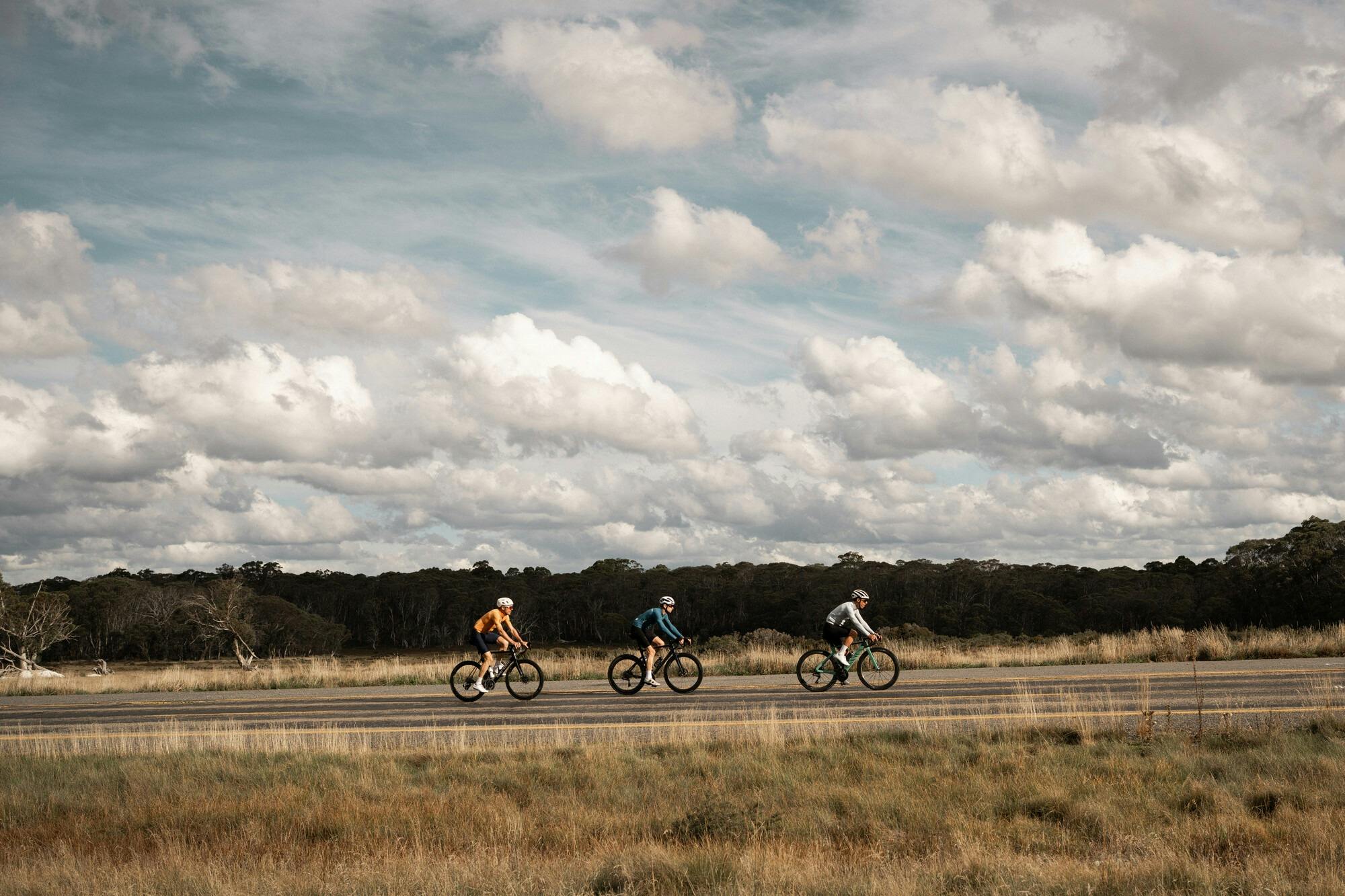 Three cyclists riding past alpine heathland on the Dinner Plain 7 Peaks Challenge route.