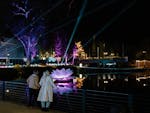 Couple views glowing lotus and lights reflecting on water at night during light festival.