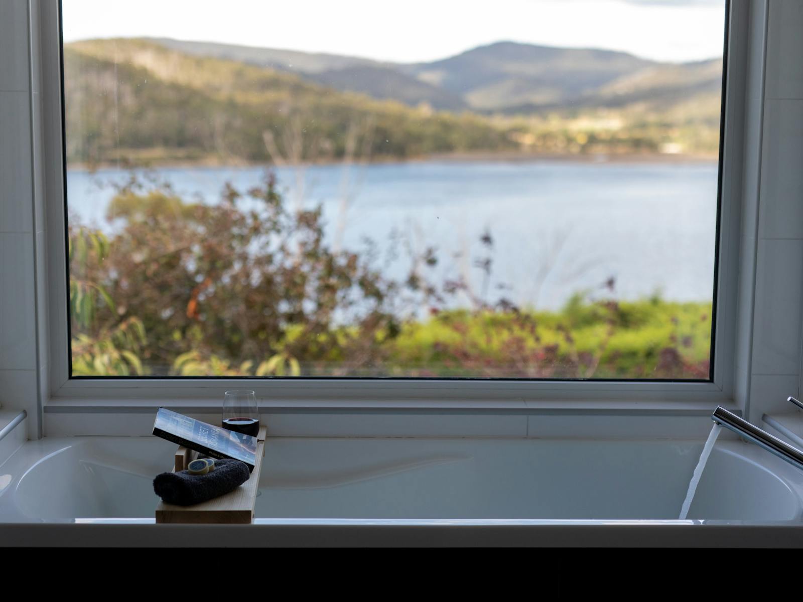 Image of a bath running with a book and a glass of wine with a view of the water in the background