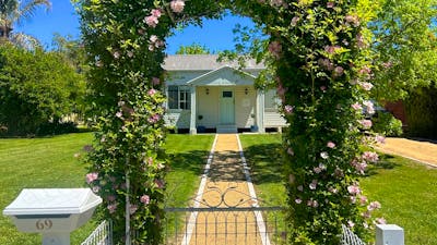 A charming cottage with a blue door, framed by a flowering vine archway and a garden path.
