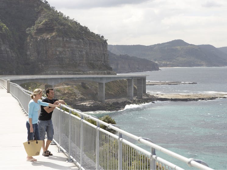 man and woman standing on seacliff bridge, leaning on rail looking out to sea