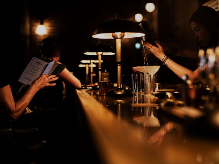 person reading menu at bar being served a cocktail