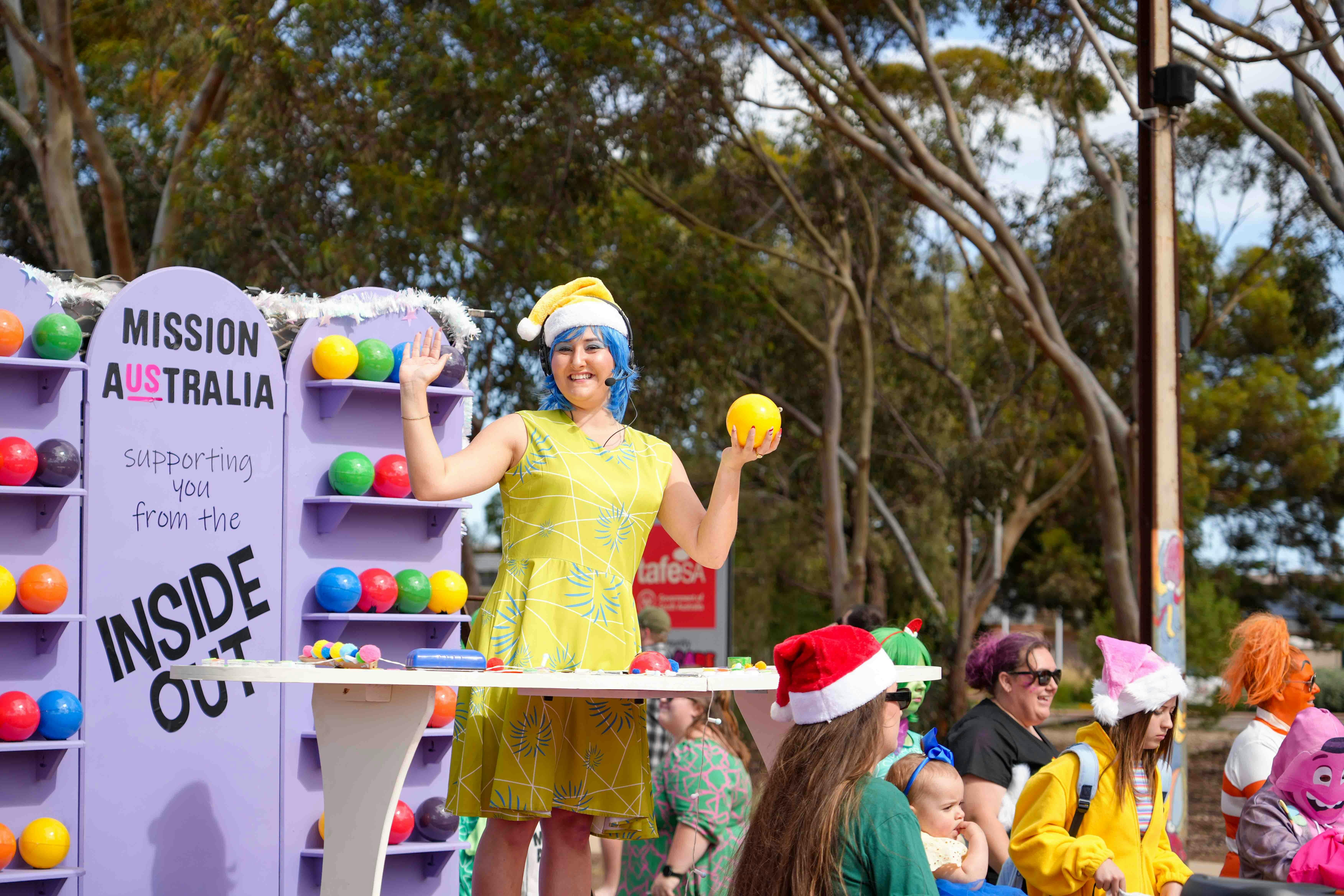 Character from Inside Out standing in a yellow dress with blue hair on the colourful float