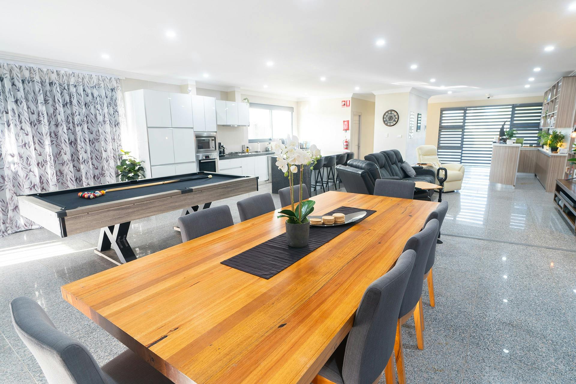 A large 8 + seat dining table in the foreground, plus pool table and kitchen lounge space