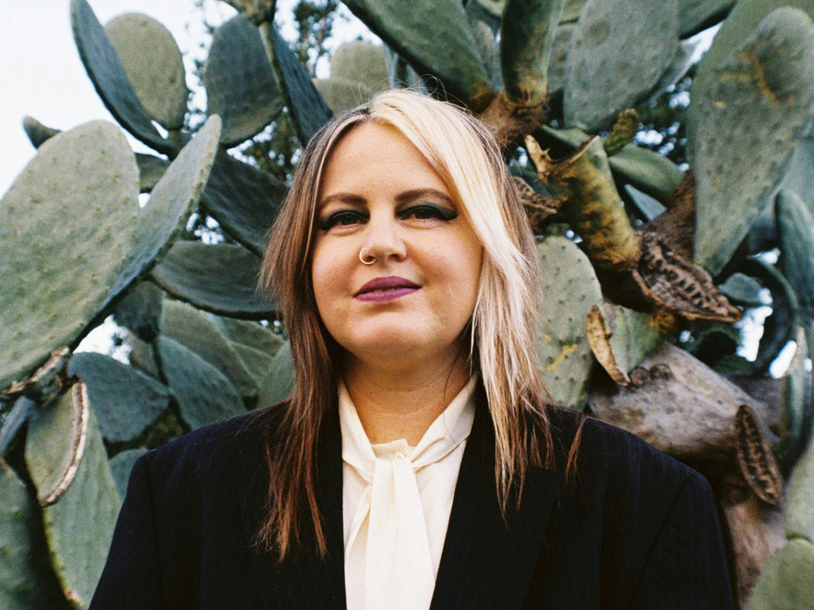 A woman in a black velvet suit standing in front of sage green cactus plants