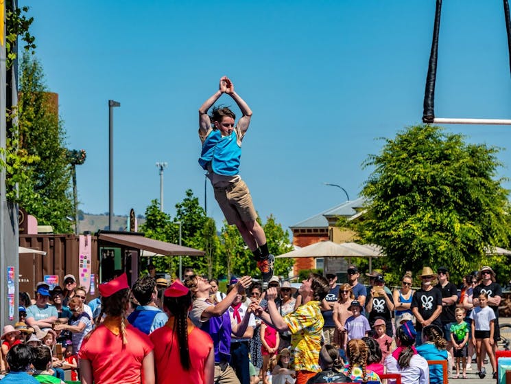 A young acrobat flies through the air as audience look on.