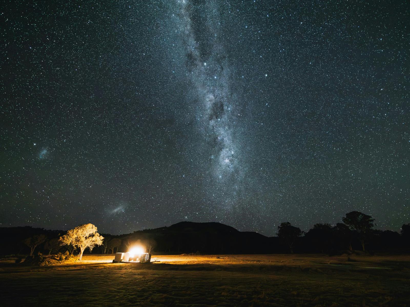 A tree and Bubbletent lit up at the base of Mount Mackenzie and under the Milky Way