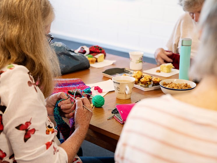 women sitting around a table filled with yarn and plates of food