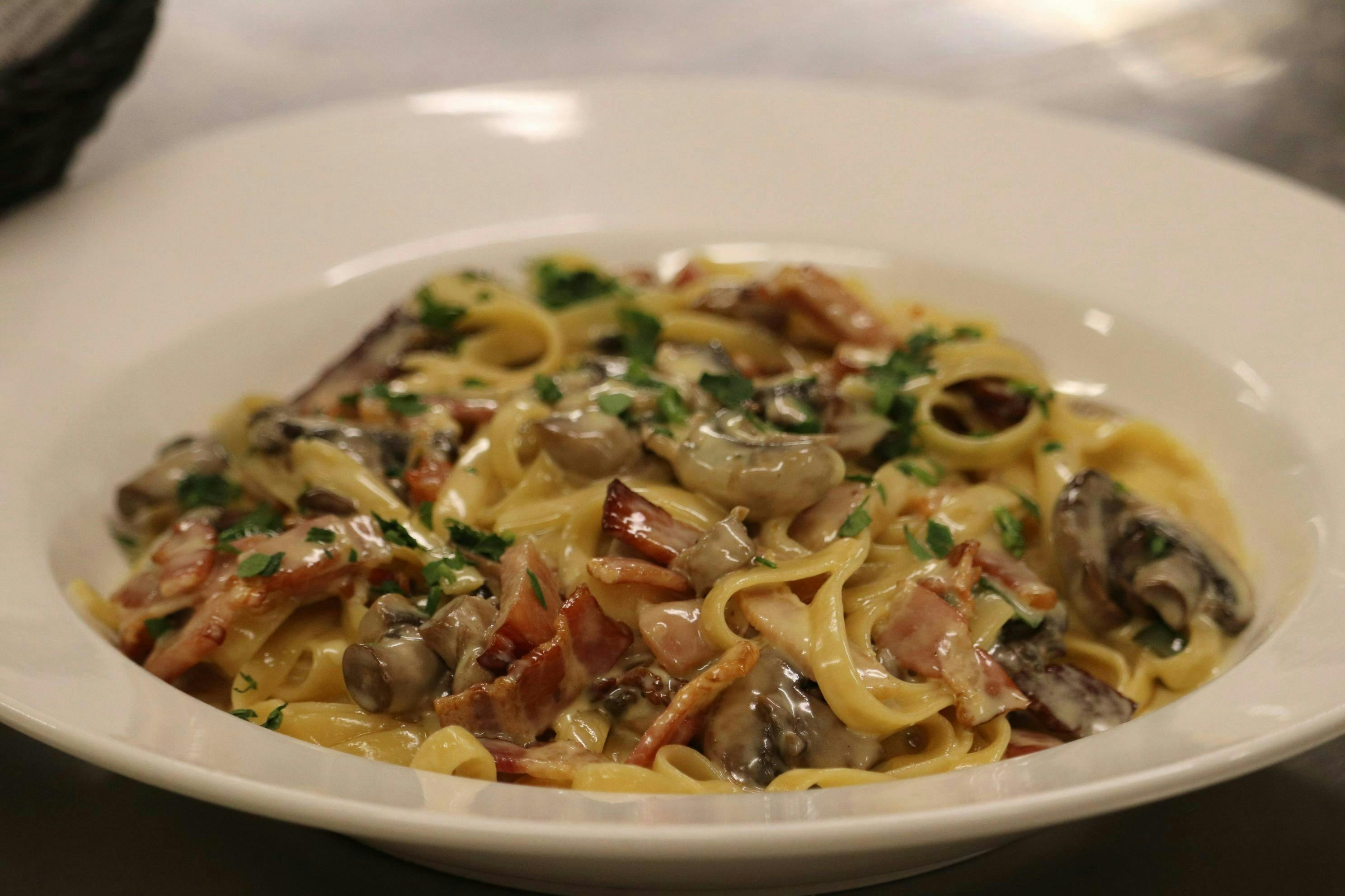 Creamy pasta with mushrooms and bacon, garnished with herbs in a white bowl