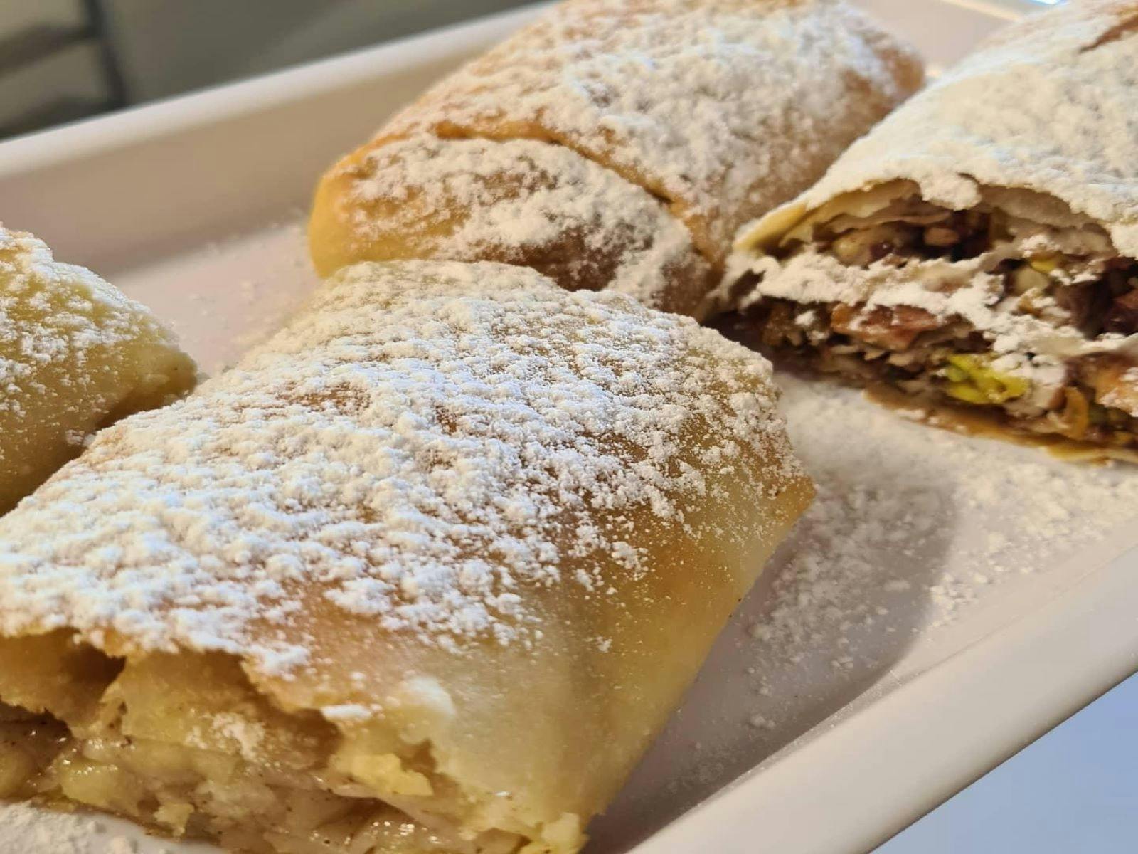 Different pastries laid out on a white plate and sprinkled with icing sugar.