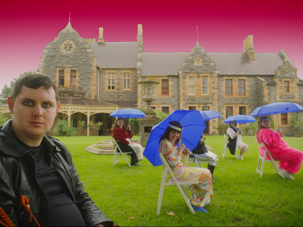 Photograph, colourfully dressed group in front of large colonial house, with bright pink sky behind