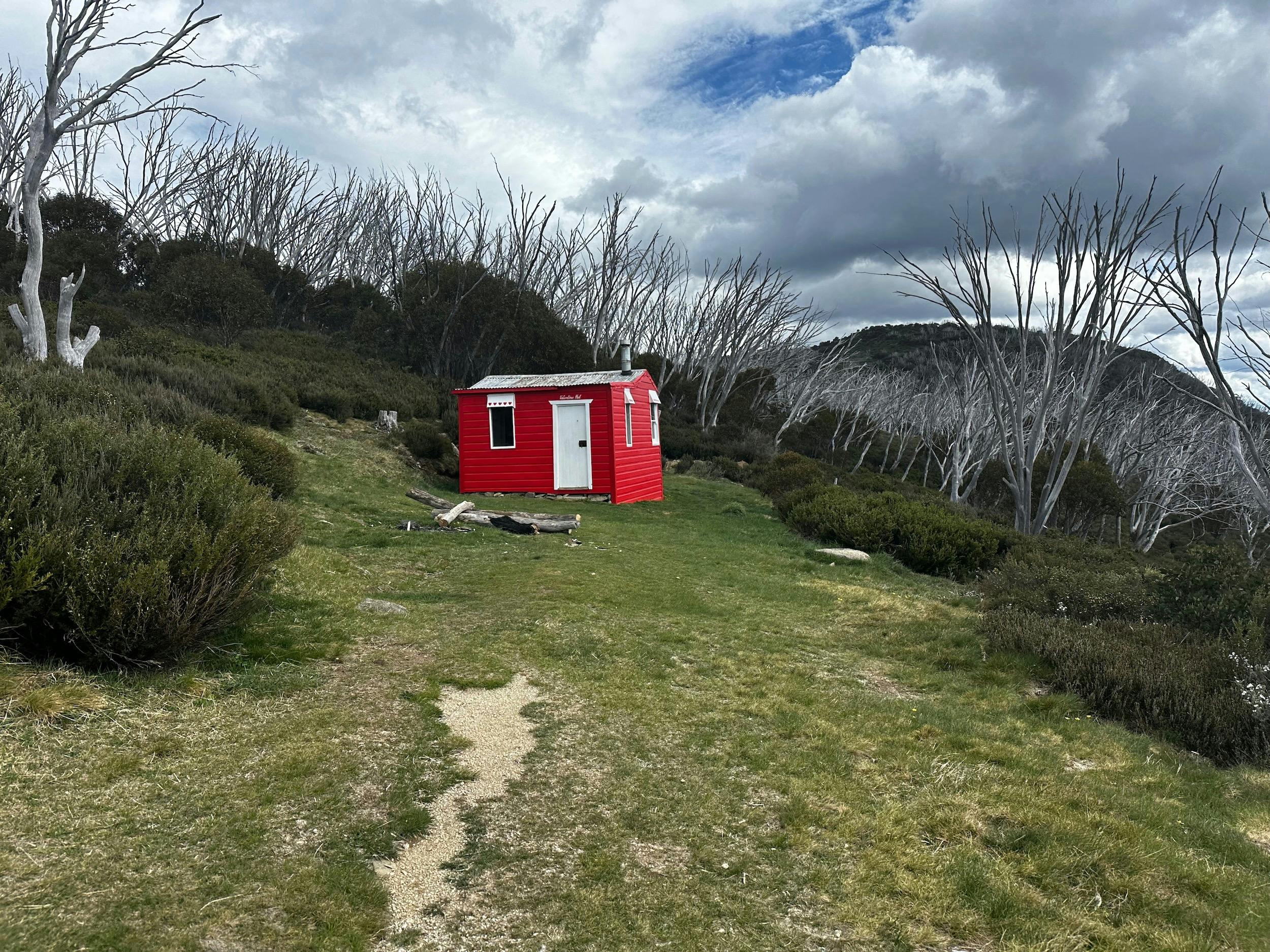 A red hut in the centre of the landscape with a mountain to the right.