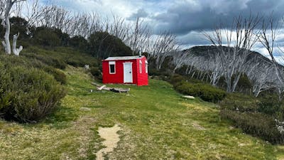 A red hut in the centre of the landscape with a mountain to the right.