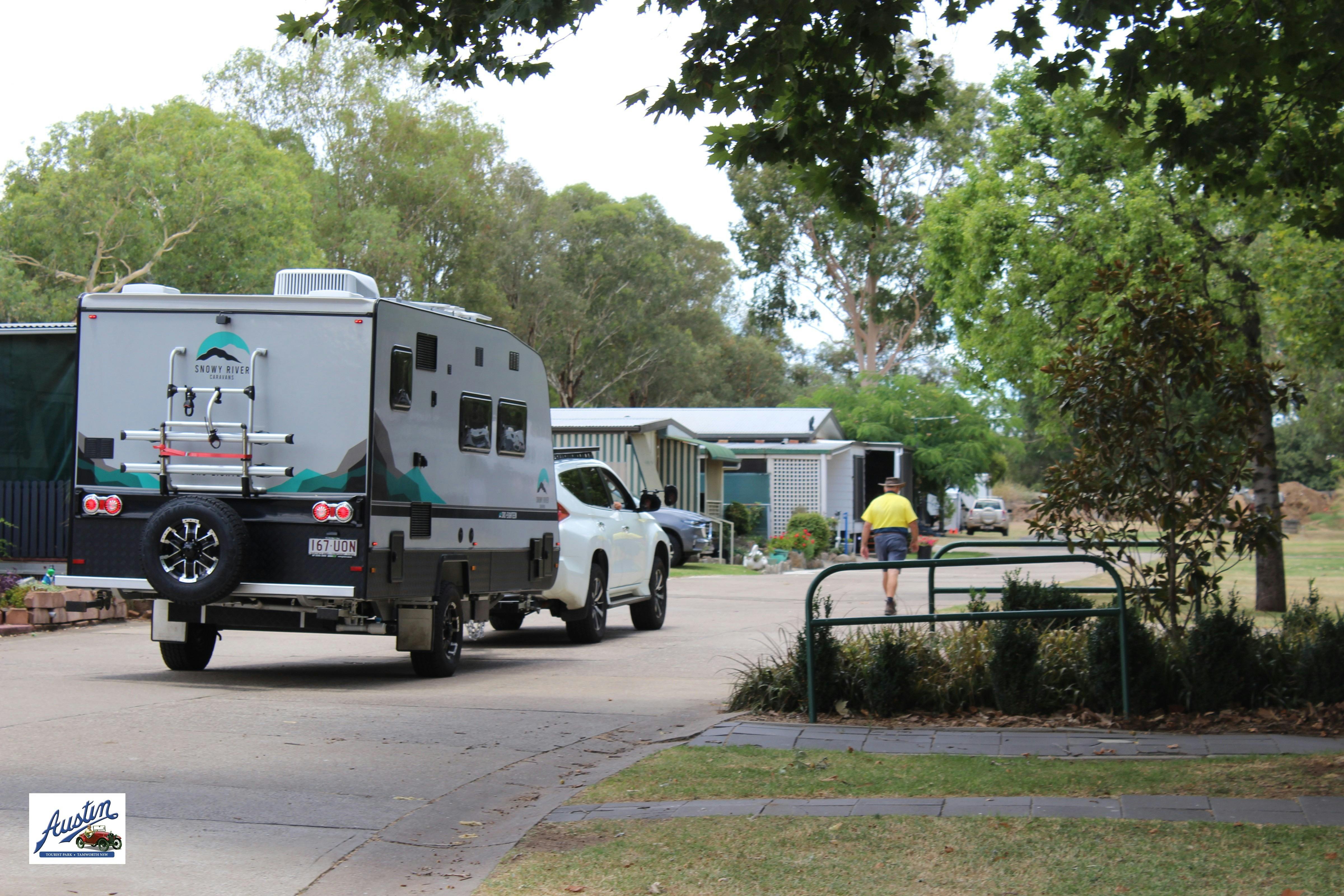 직원이 캐러밴을 공원으로 안내하여 현장에 주차하고 있습니다. 푸른 나무와 정원이 아름답습니다.