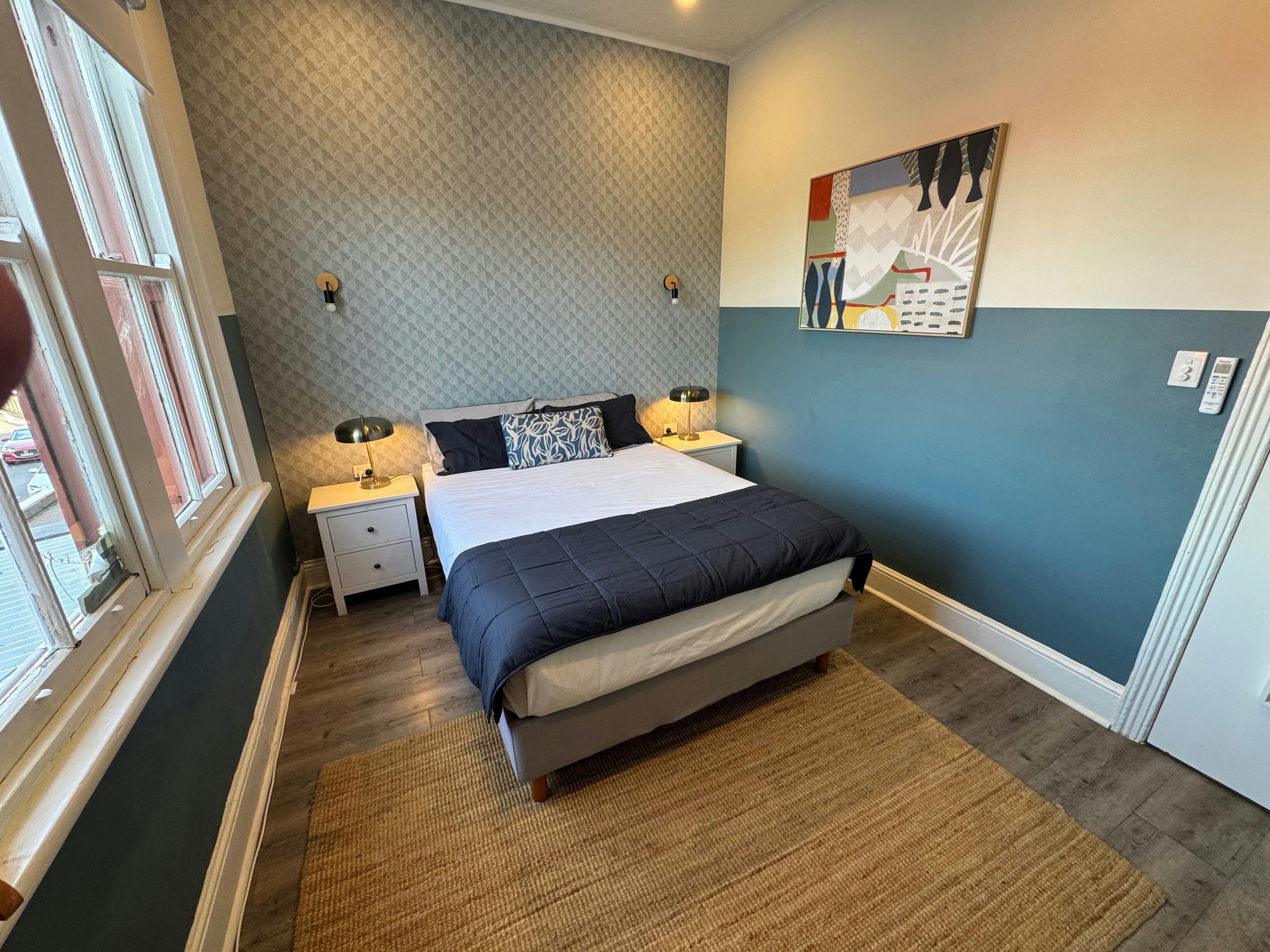 Guest room at Native Rose Hotel with a queen bed, bedside tables, large windows and contemporary blu