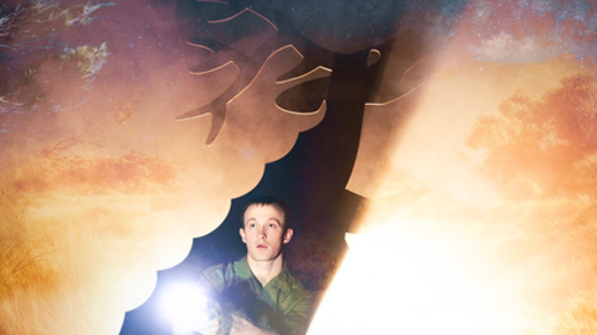 A young man is shining a torch in the bush, revealing the outline of a deer with big antlers