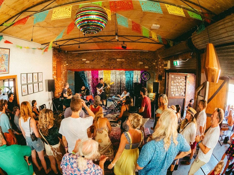 arial view of a crowded room with people listening to a band play guitar, drums & keyboard