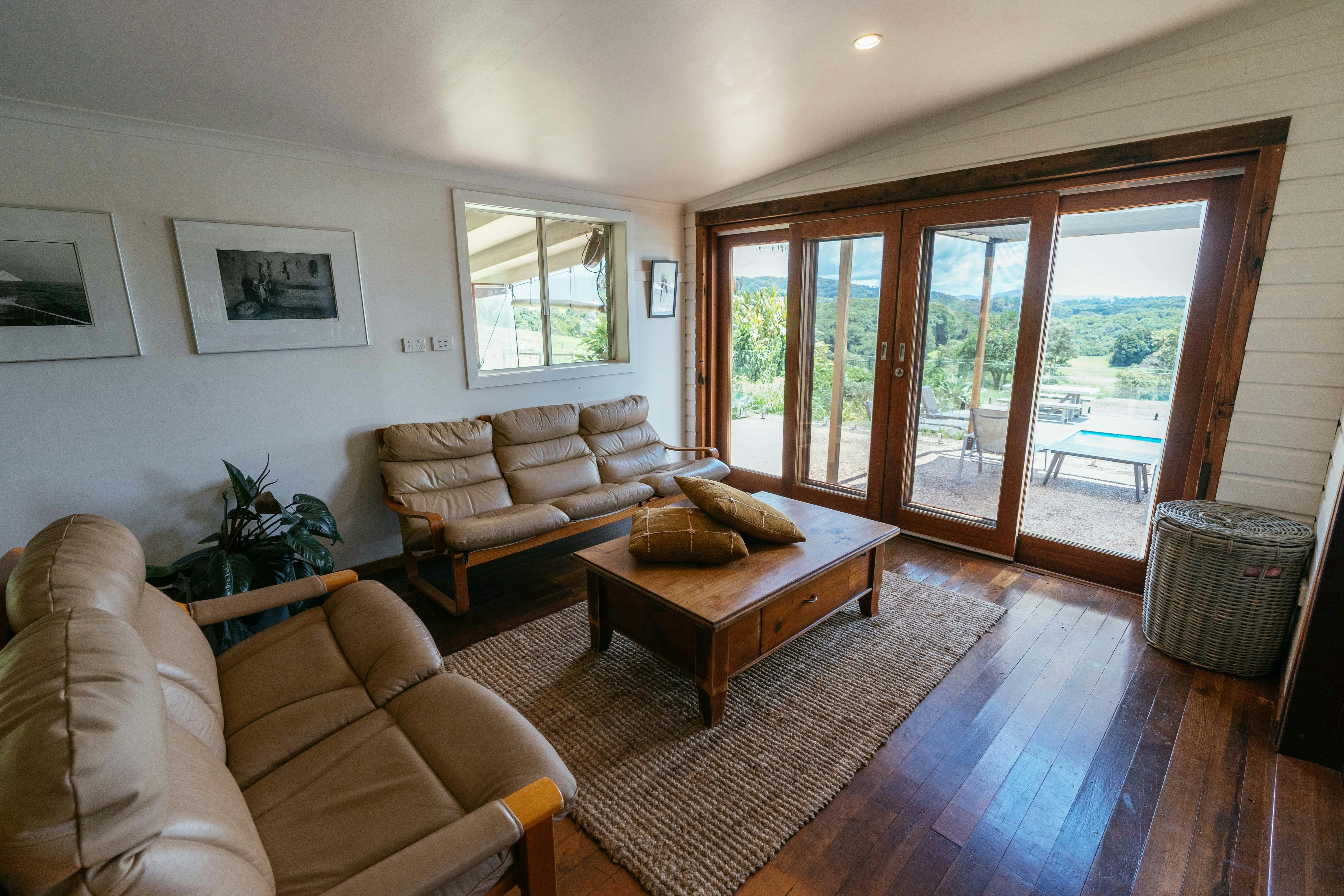 Two large lounges face a window that overlooks a green valley, a pool area and hot tub in Byron Bay