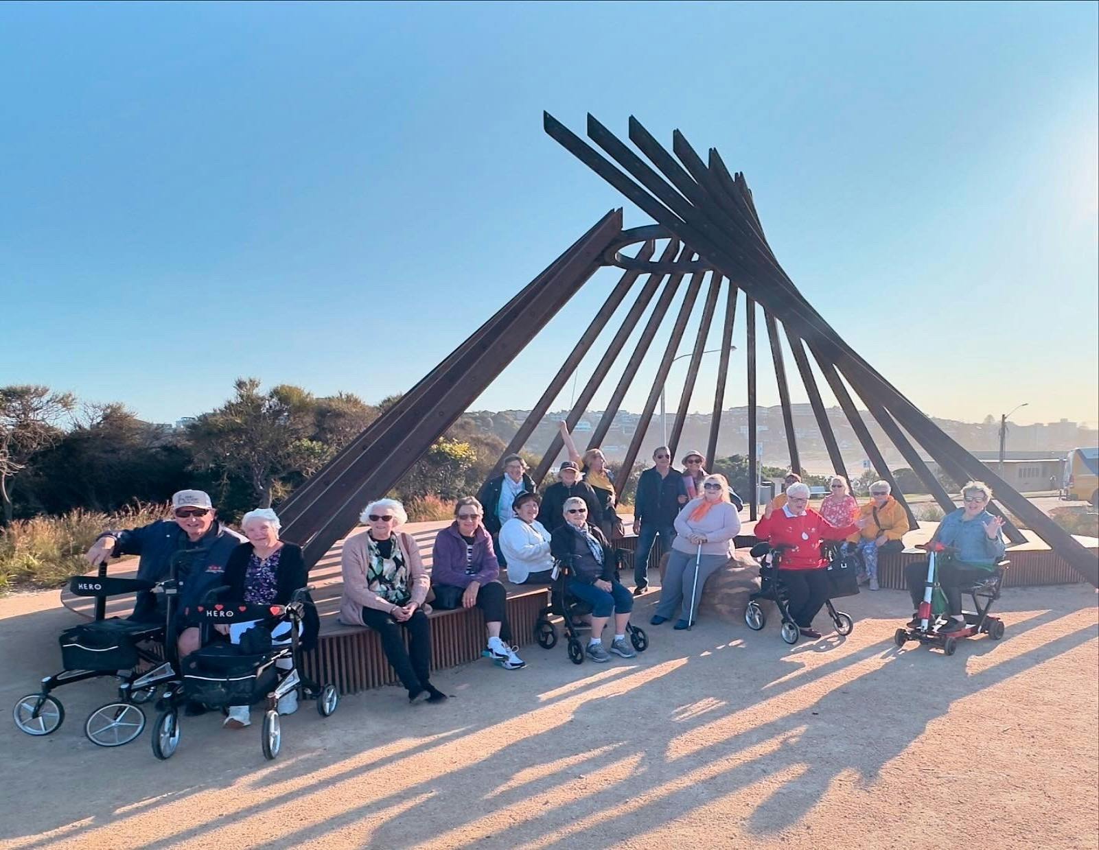 アクセシブルツアーに参加した大勢のグループが、狼煙記念碑の下に座っています。