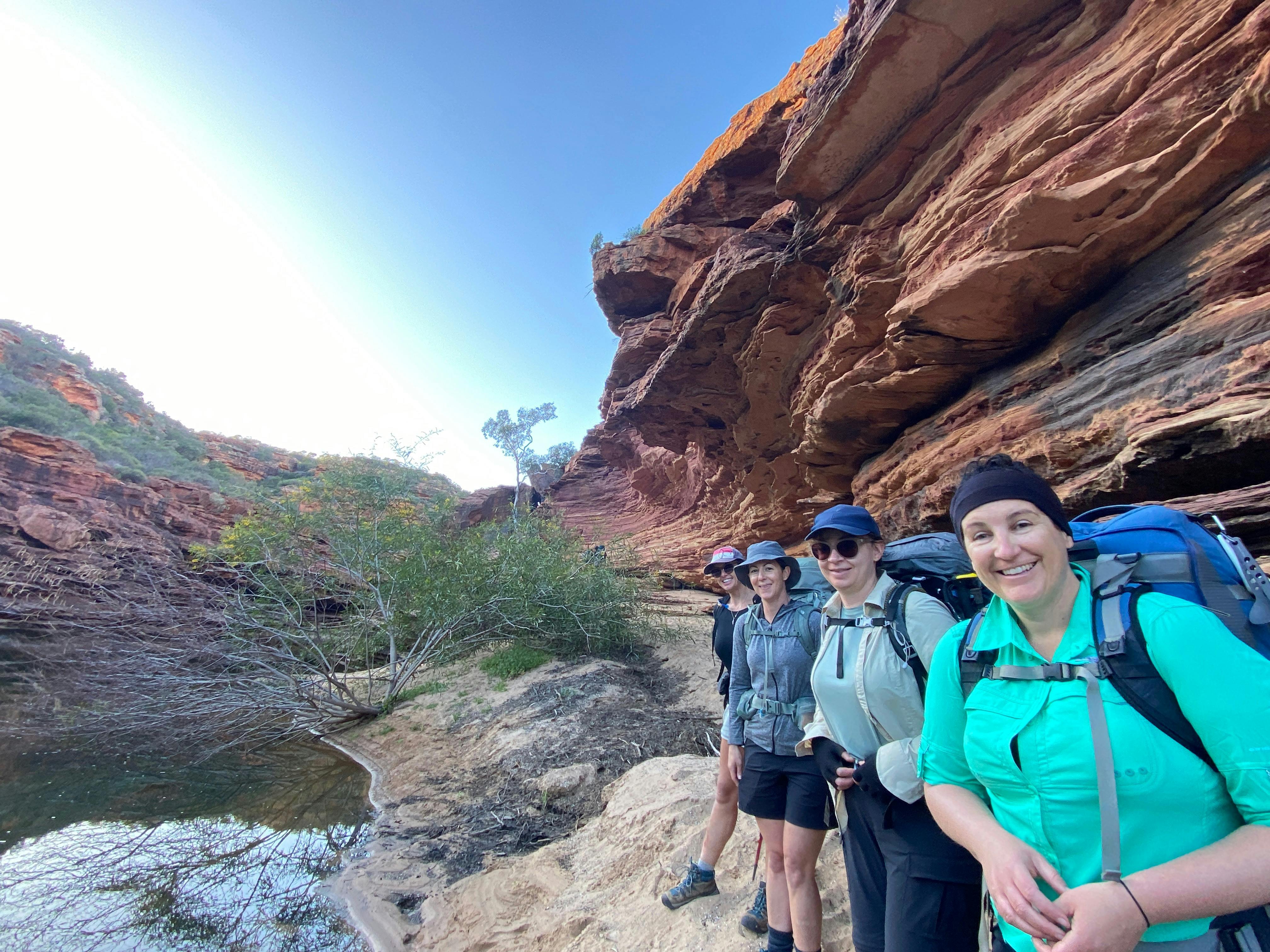 four women line up by the sandstone walls of gorge about to start wading in the river