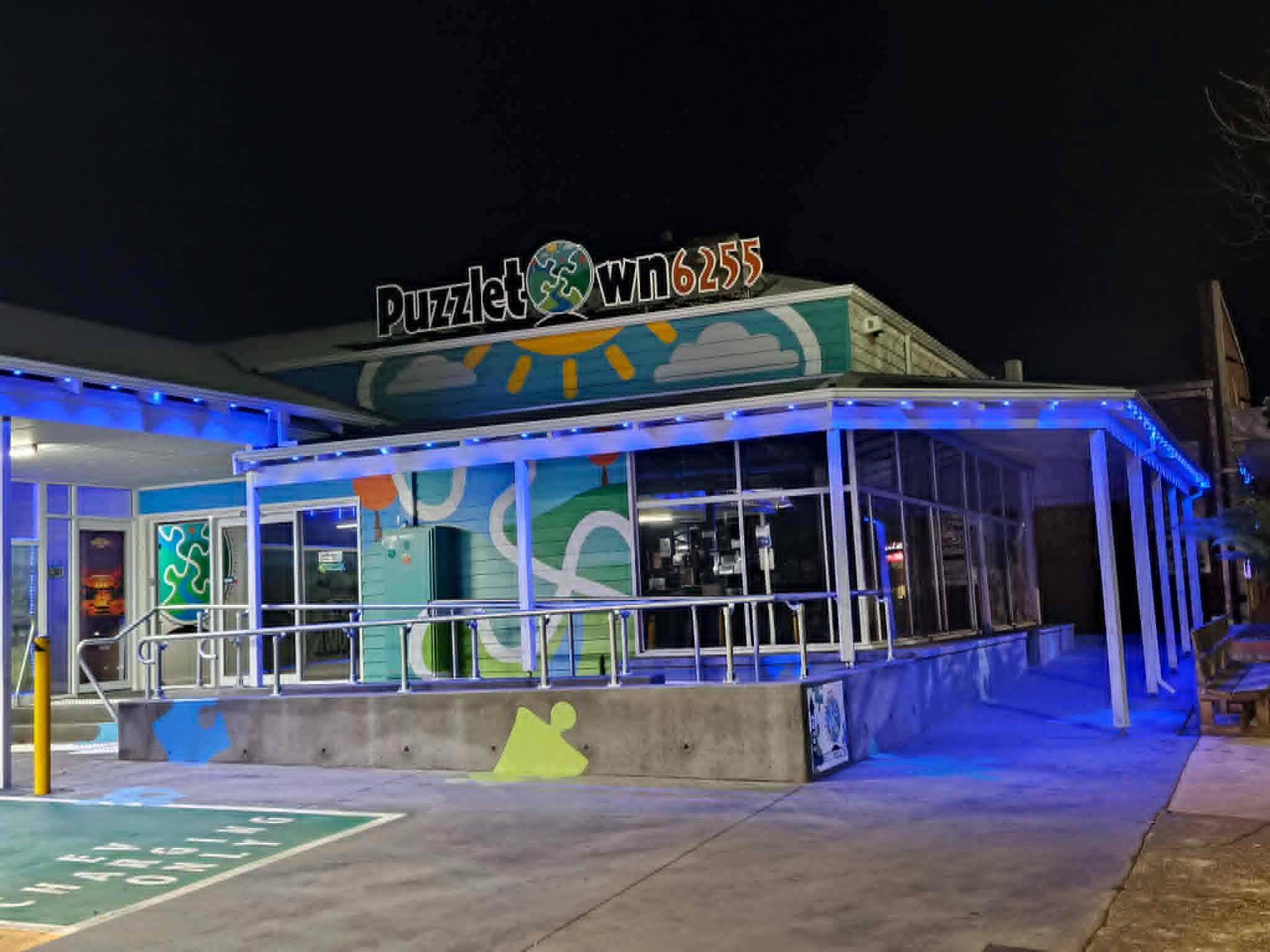 Puzzletown6255 at night, with blue lights and logo against the night sky