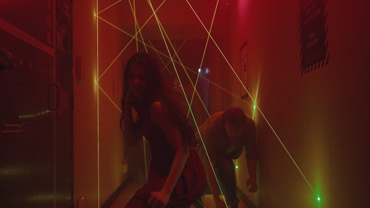 Three people weaving through a hallway filled with green lasers.  An ominous red glow fills the room