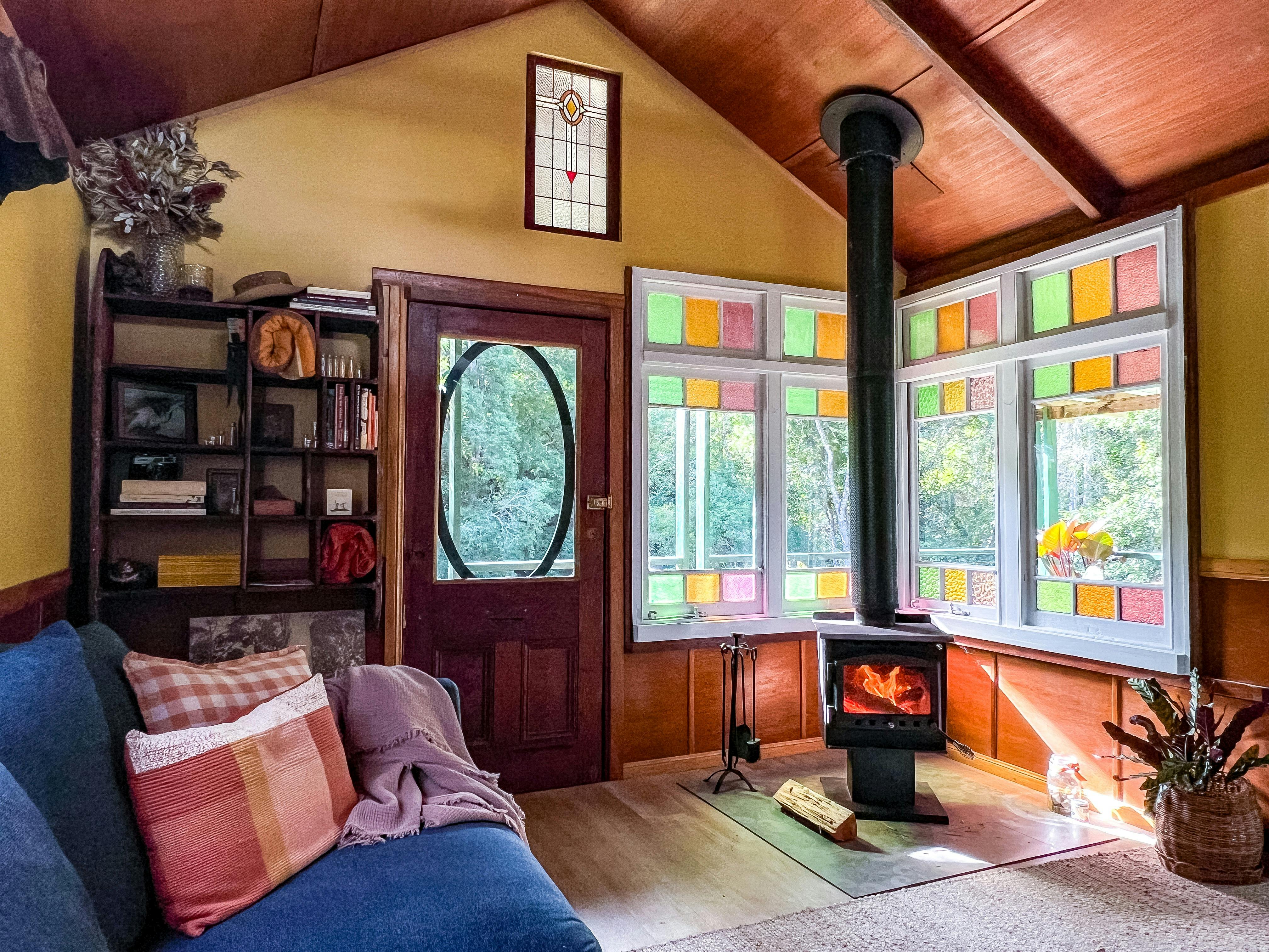 A yellow room with stained glass windows and a firplace is bathed in sunlight with a bookshelf.