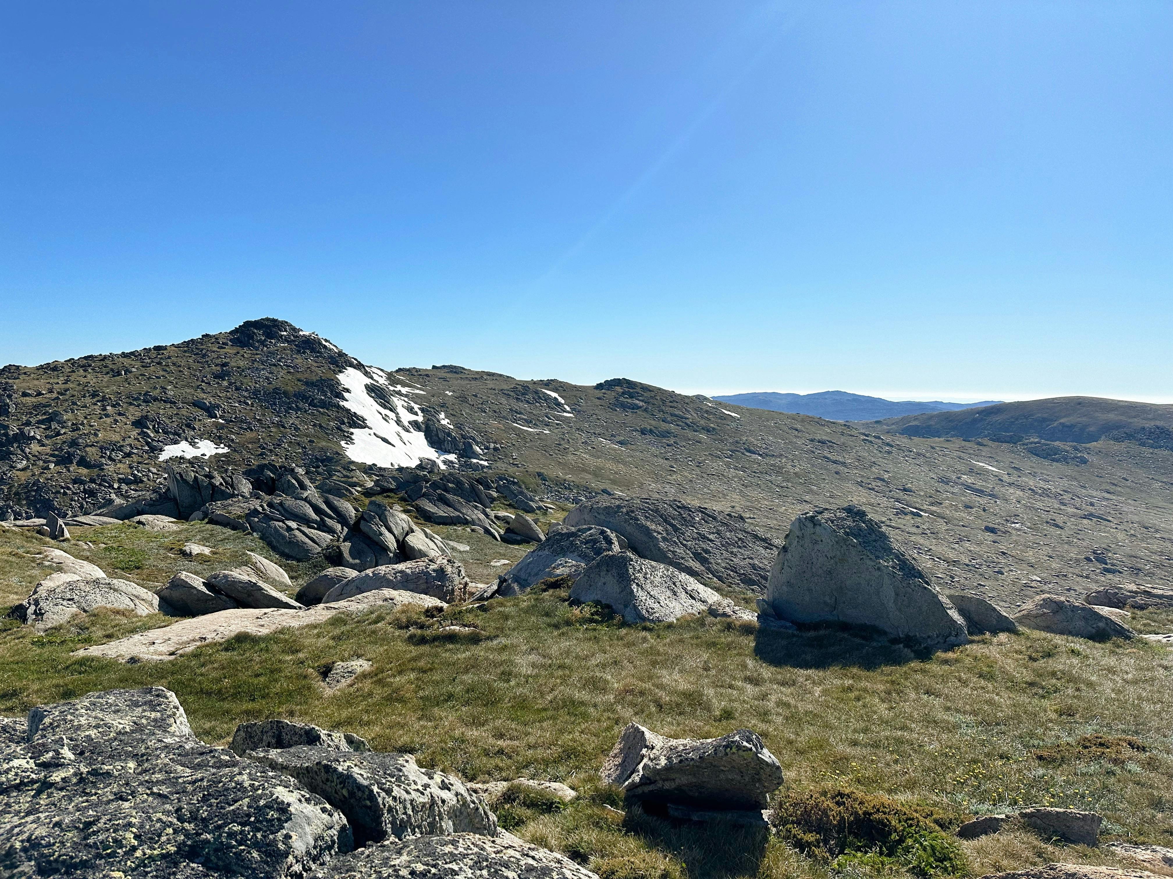 Large boulders in the mountains with some snow on a peak behind it.