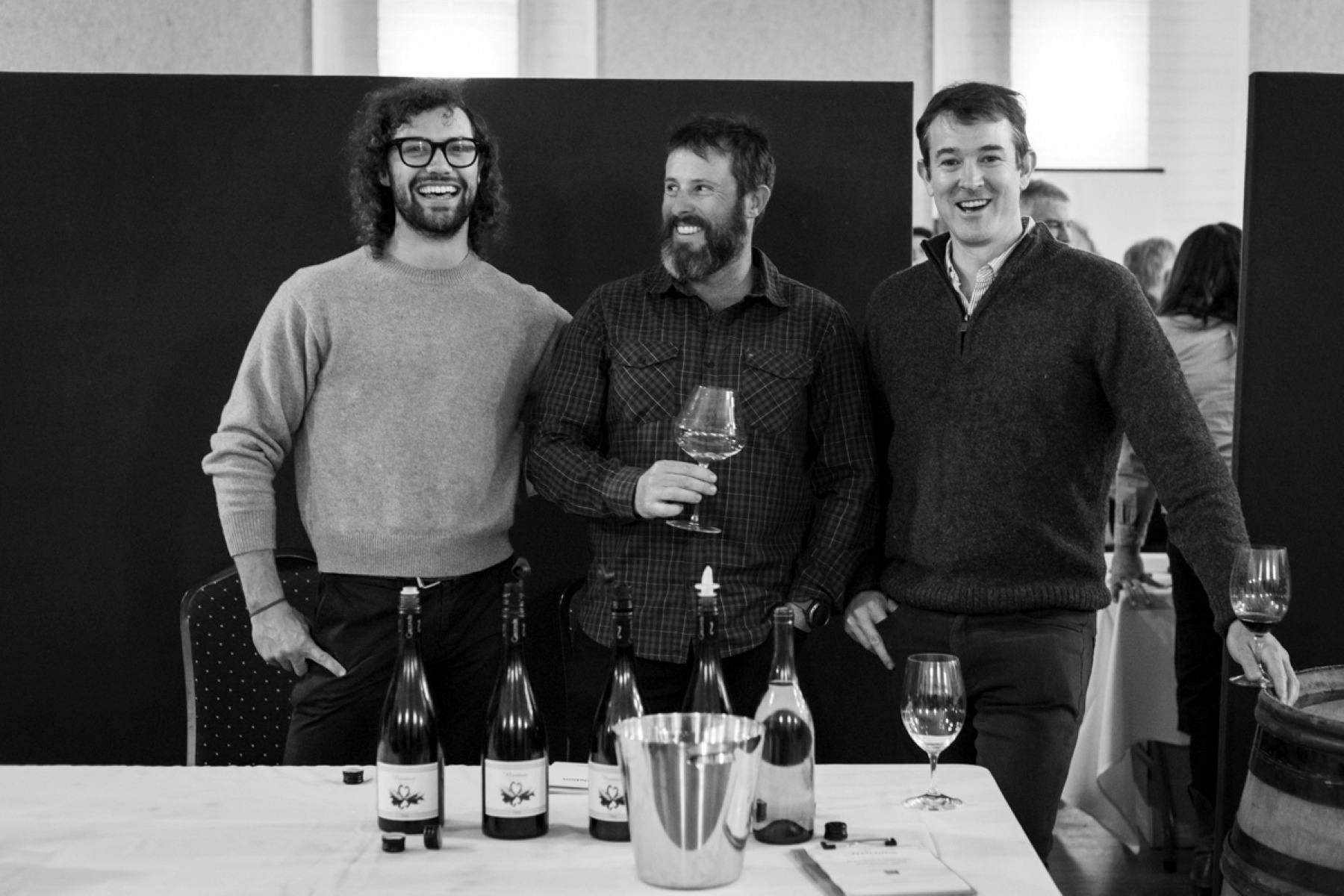 Three men posing with wine bottles