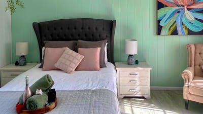 A cozy bedroom for two with pastel pink cushions, mint green walls, and vibrant floral artwork.