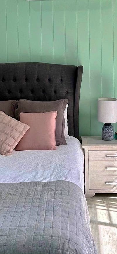 A cozy bedroom for two with pastel pink cushions, mint green walls, and vibrant floral artwork.