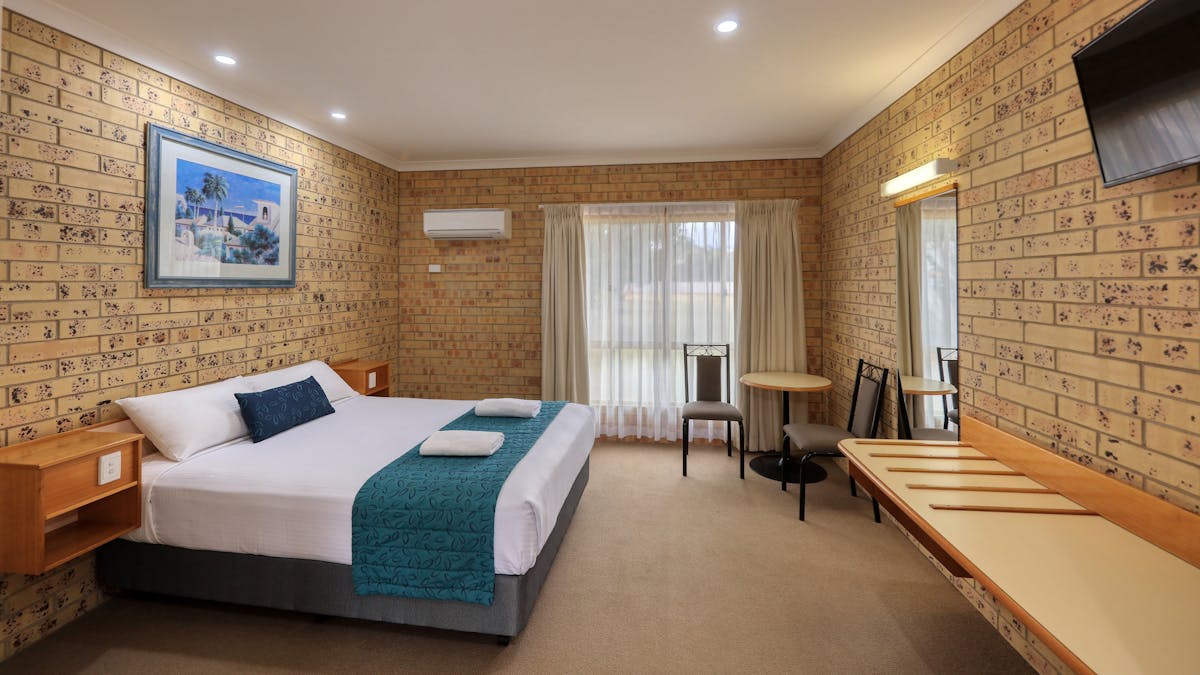 Room photo showing 1 queen bed, tables and chairs, bench and window