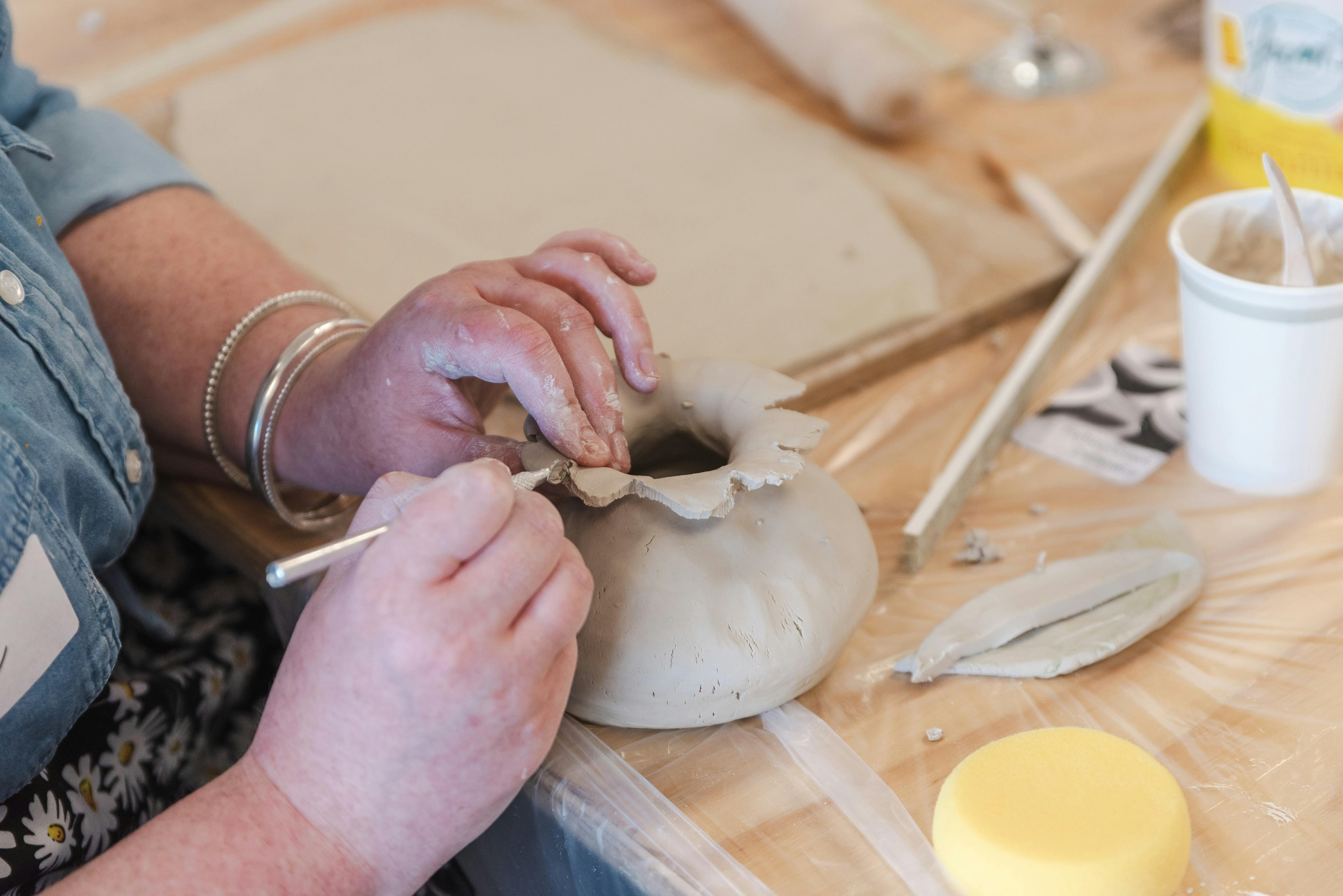 A workshop participant uses small tools to carefully add detail to their handmade ceramic vase