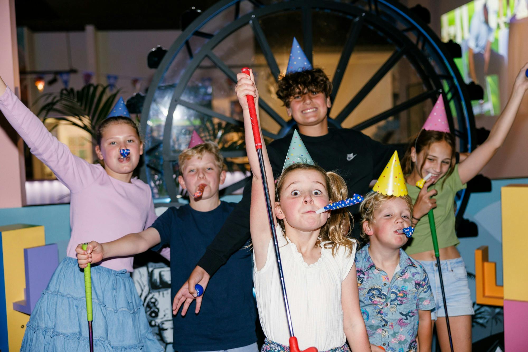 a group of children wearing party hats celebrate while playing mini-golf
