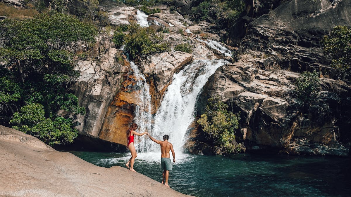 A couple sit on a granite boulder overlooking the waterfalls at Emerald Creek Falls in Mareeba TNQ.